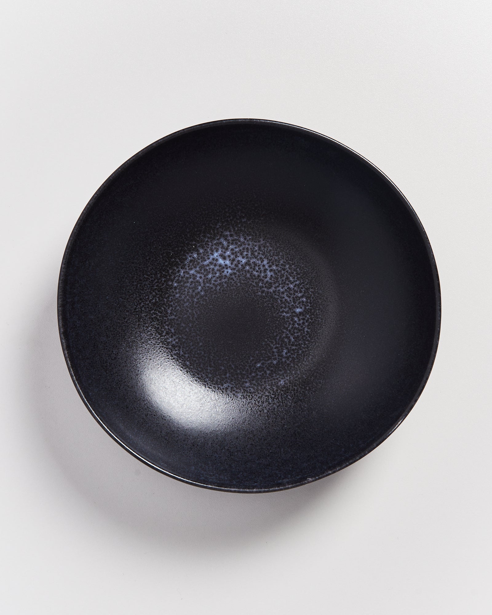 Dunkler, runder Teller mit einer gesprenkelten Textur auf einer weißen Oberfläche.