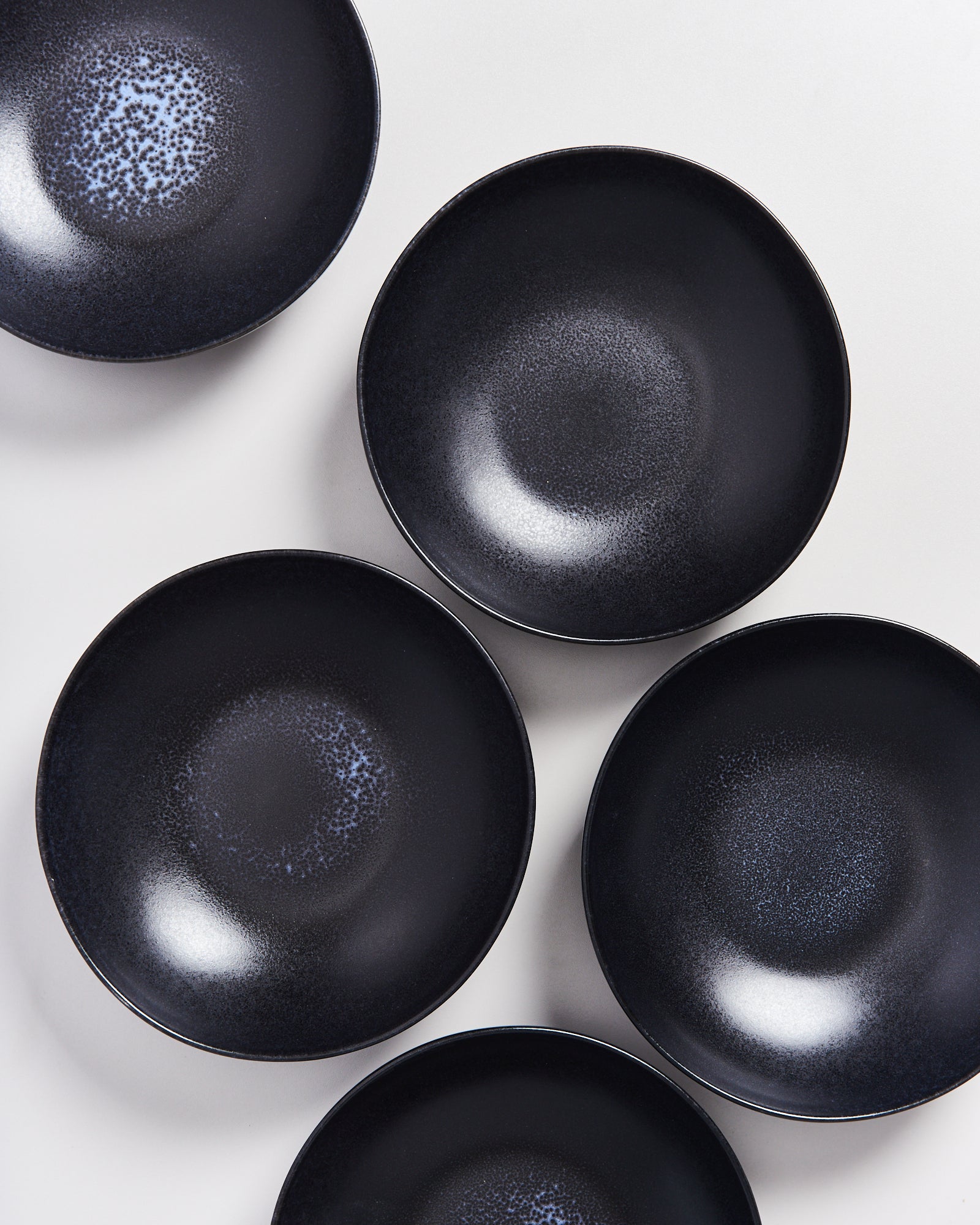 Fünf schwarze Teller mit einem dezenten, gesprenkelten Muster auf einem weißen Hintergrund.