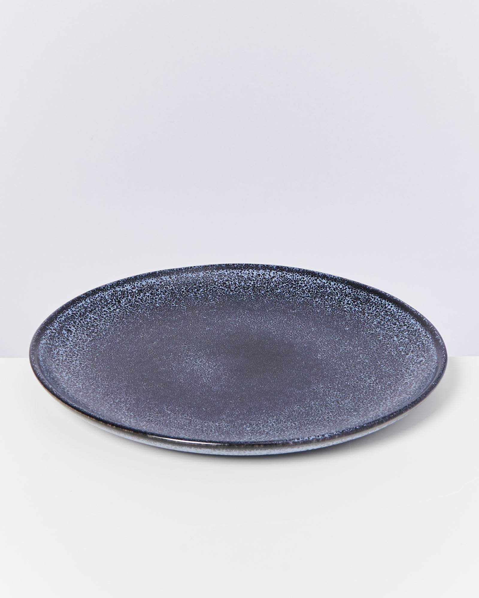 Ein dunkelblauer Keramikteller mit gesprenkeltem Muster auf einem weißen Hintergrund.
