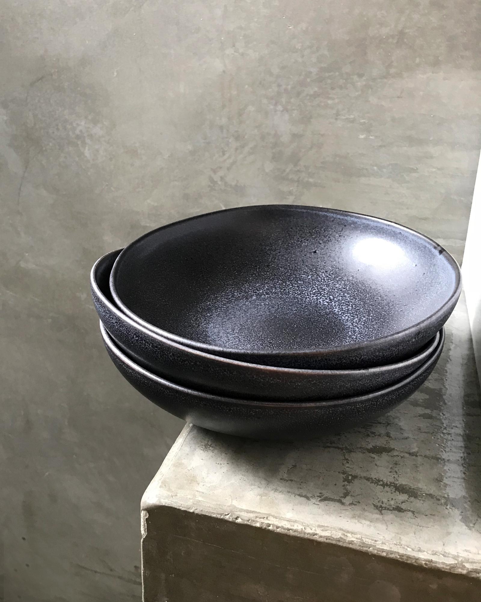 Drei stapelbare schwarze Schüsseln auf einem Betonuntergrund vor einer strukturierten grauen Wand.