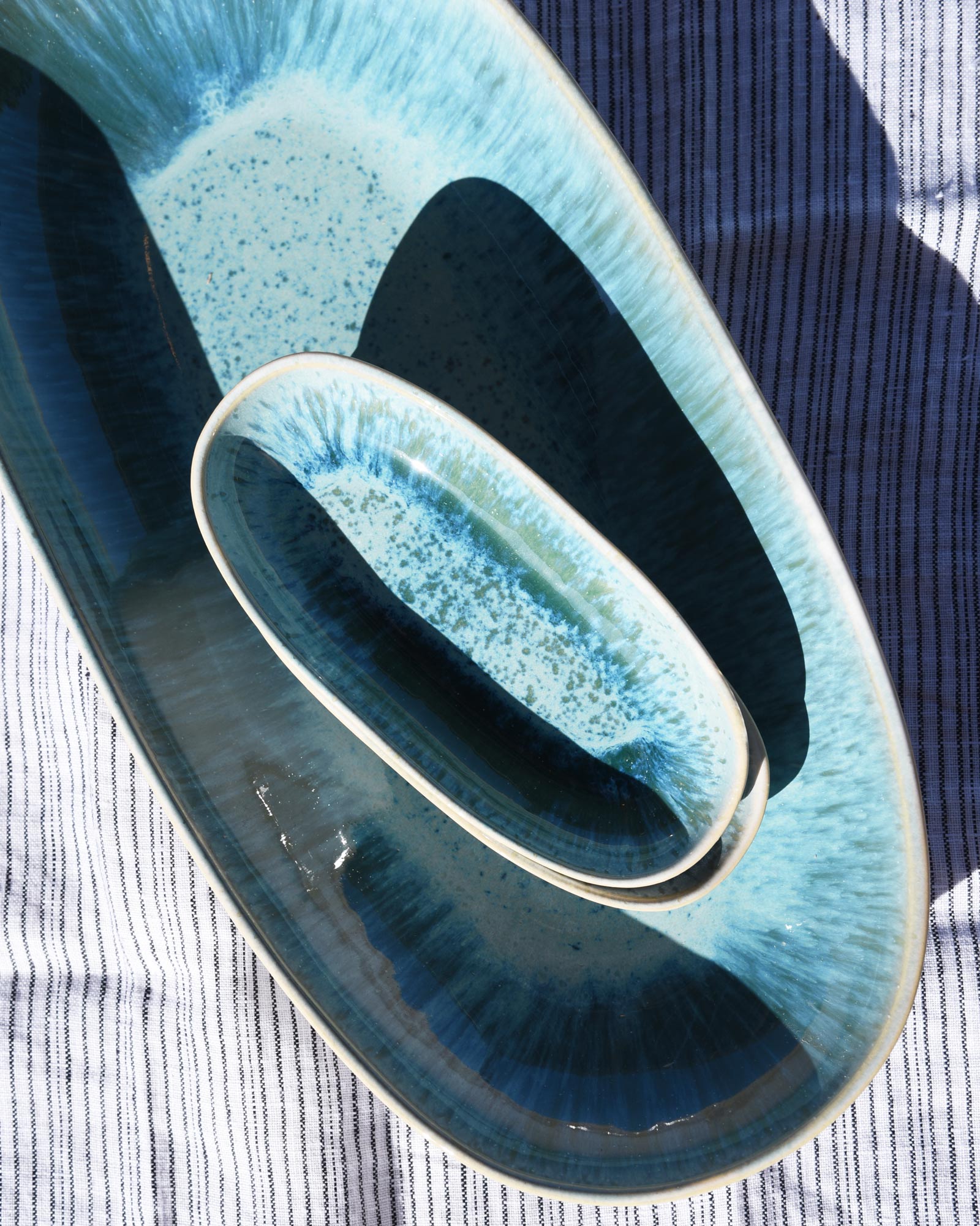 Zwei grün-blaue Keramikteller in verschiedenen Größen auf einem gestreiften Stofftuch.