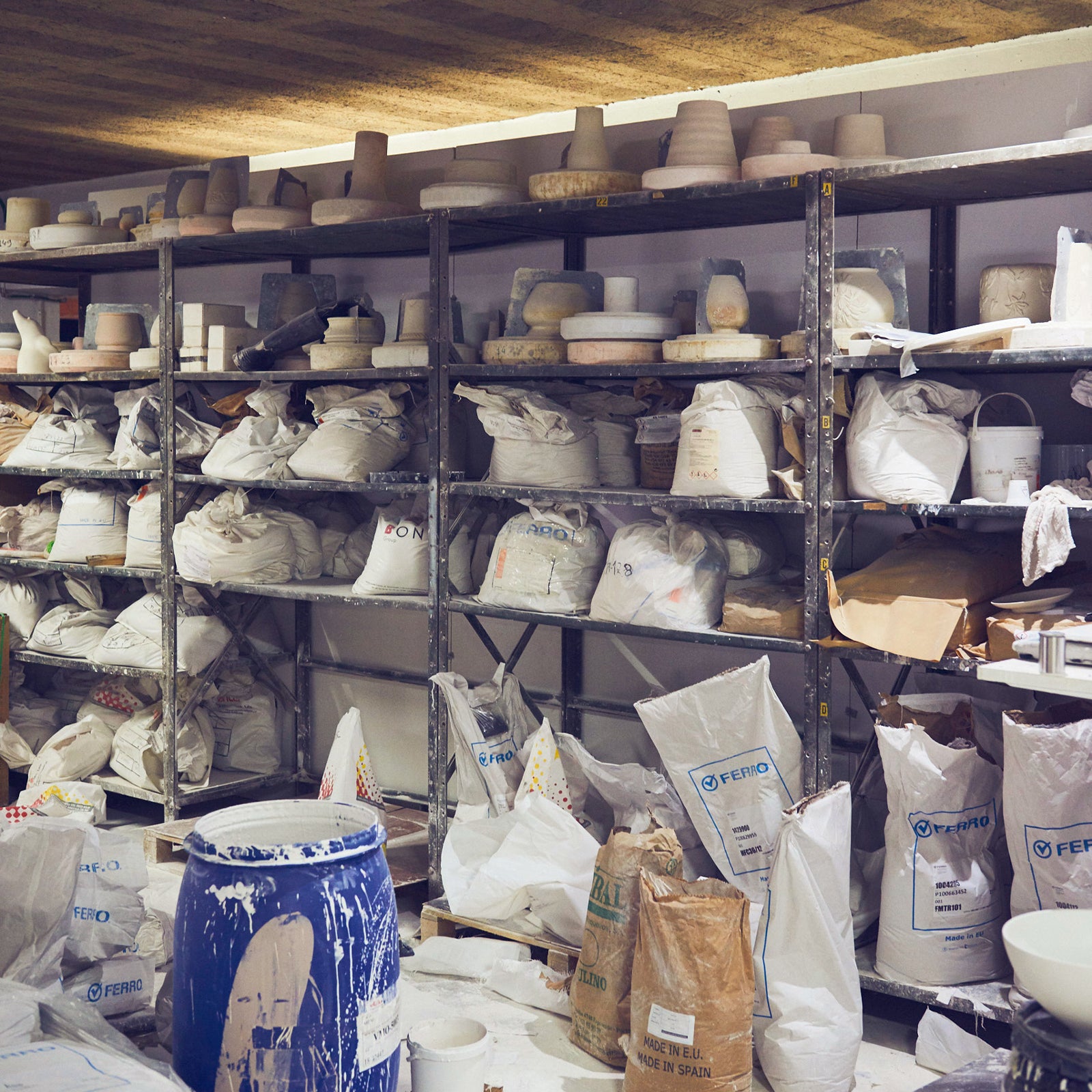 Regale mit Tonwaren, Säcken und Fässern in einer Werkstatt.