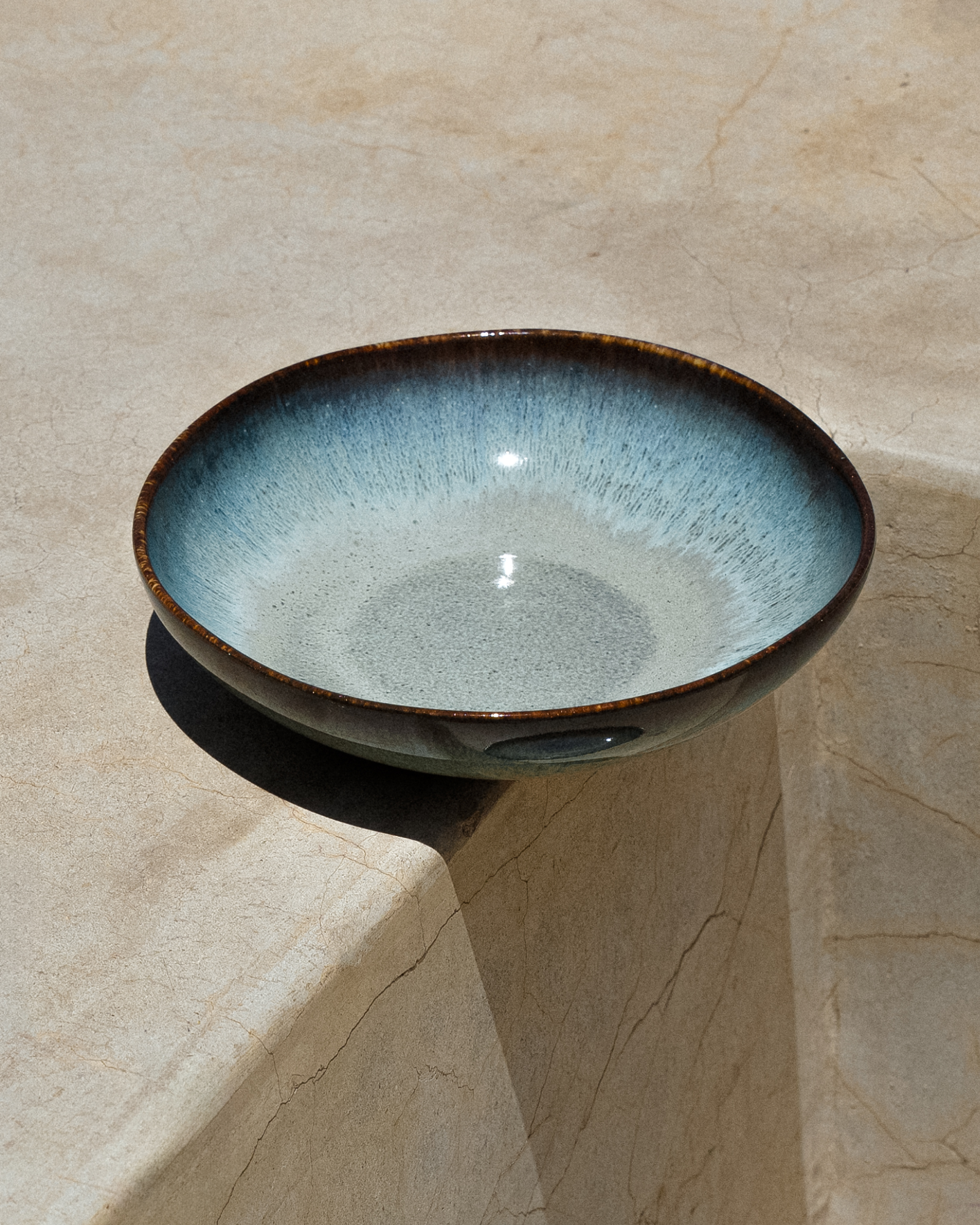 Keramikschale mit blauem und braunem Rand steht auf einer steinernen Oberfläche im Sonnenlicht.