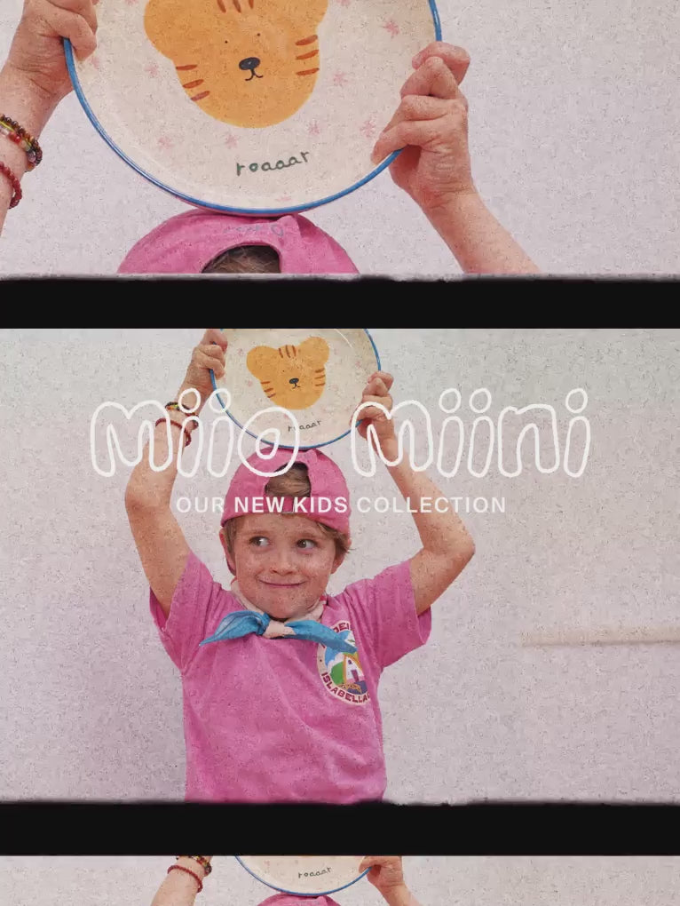 Ein Kind hält einen Teller mit einem Tigerkopf-Motiv hoch. Text: "mio miini OUR NEW KIDS COLLECTION".