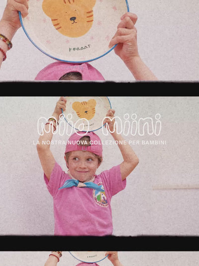 Kind in rosa Kleidung hält einen Teller mit Tierillustration, darüber der Text "Miio Miini" und "La nostra nuova collezione per bambini".