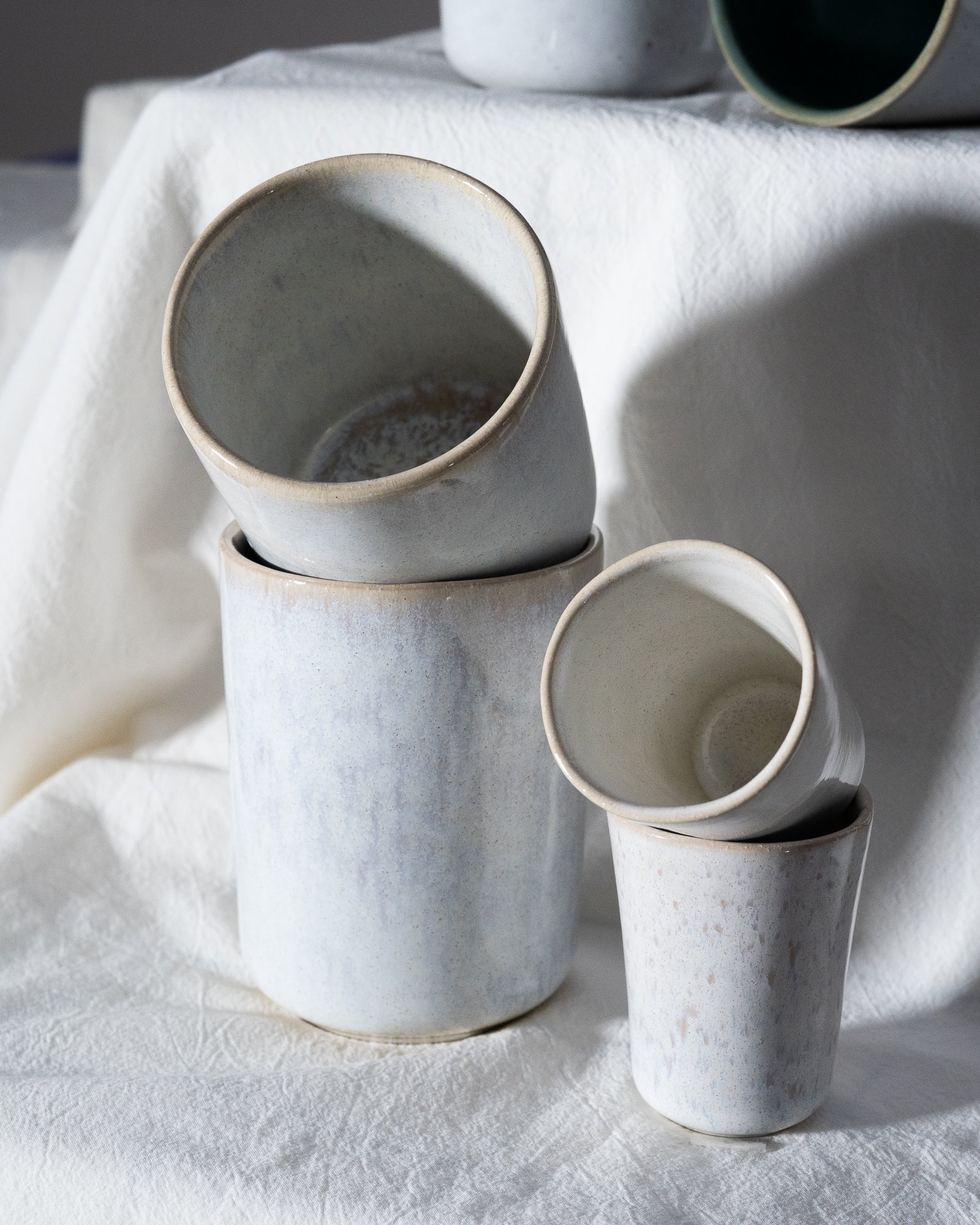 Vier stapelbare Keramikbecher in gedeckten Farben auf einem weißem Tuch arrangiert.